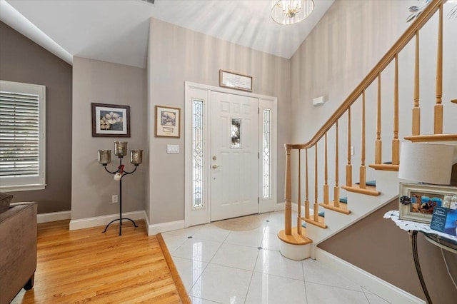 entrance foyer with high vaulted ceiling, stairway, baseboards, and light tile patterned floors