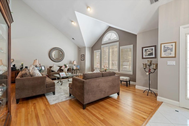 living area with light wood-type flooring, baseboards, visible vents, and high vaulted ceiling