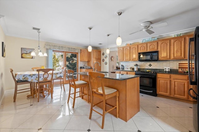 kitchen with brown cabinetry, pendant lighting, a center island with sink, and black appliances