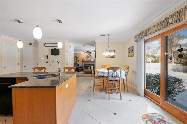 kitchen featuring dark stone counters, dishwasher, decorative light fixtures, a kitchen island with sink, and a sink