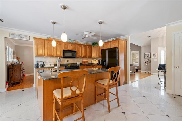 kitchen featuring light tile patterned floors, a sink, black appliances, an island with sink, and pendant lighting