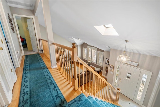 hall with lofted ceiling with skylight, an upstairs landing, and an inviting chandelier