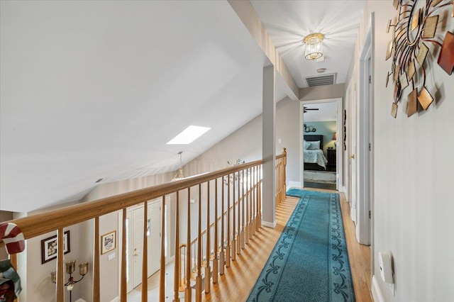 corridor featuring light wood-type flooring, vaulted ceiling with skylight, visible vents, and an upstairs landing