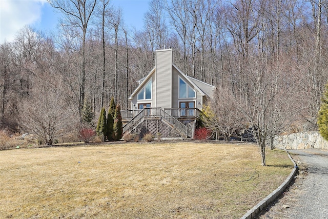 view of front of property with a chimney, a view of trees, a front yard, a wooden deck, and stairs