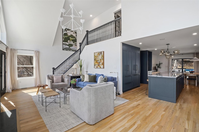 living room with a notable chandelier, light wood-style flooring, stairway, and a towering ceiling