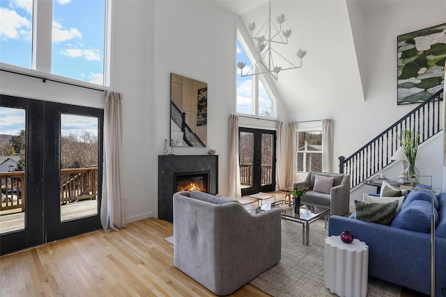 living room with stairway, an inviting chandelier, light wood-style flooring, a high end fireplace, and french doors