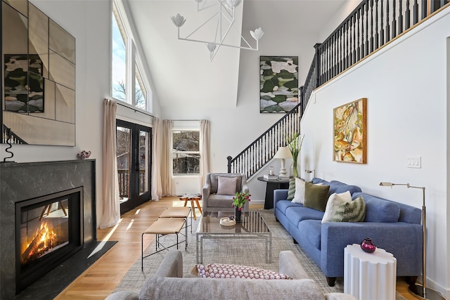 living room featuring a high end fireplace, stairway, french doors, a towering ceiling, and wood finished floors