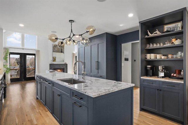 kitchen with light wood-type flooring, an island with sink, a sink, light stone counters, and a fireplace