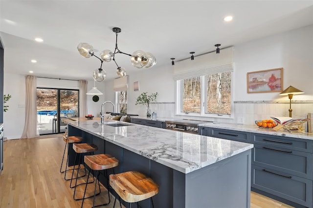 kitchen featuring a breakfast bar, light stone countertops, light wood finished floors, and a sink