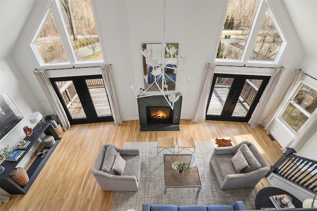 living room featuring wood finished floors, a high ceiling, a fireplace with flush hearth, and french doors