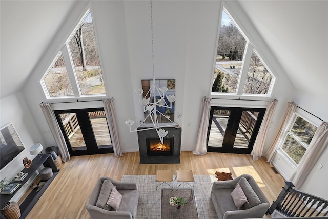 living room with french doors, high vaulted ceiling, a warm lit fireplace, and wood finished floors