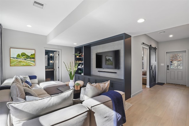 living room with visible vents, recessed lighting, light wood-type flooring, and a barn door