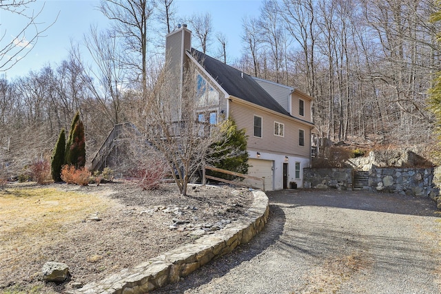 view of property exterior with stairway, an attached garage, a chimney, and driveway