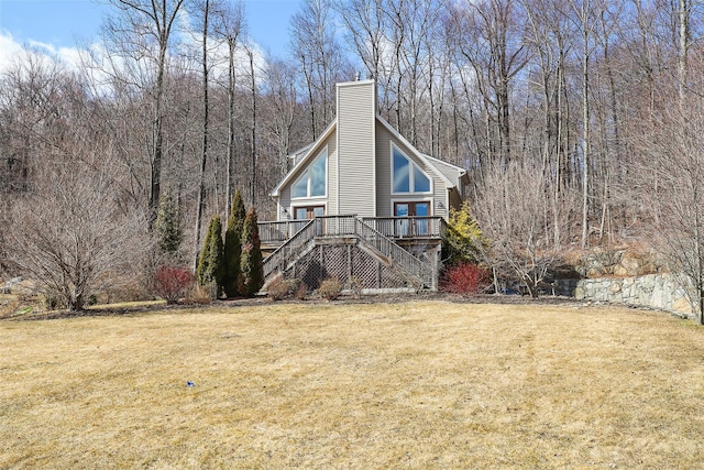 view of front of property featuring a front yard, stairway, a wooded view, a wooden deck, and a chimney