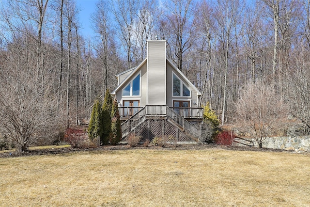 view of side of property with a lawn, a deck, stairway, a wooded view, and a chimney