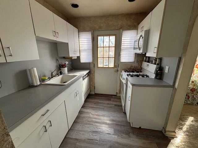 kitchen featuring stainless steel microwave, white cabinets, a sink, wood finished floors, and white range with gas stovetop