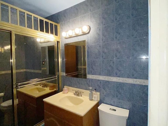 bathroom with toilet, tile walls, two vanities, and a sink