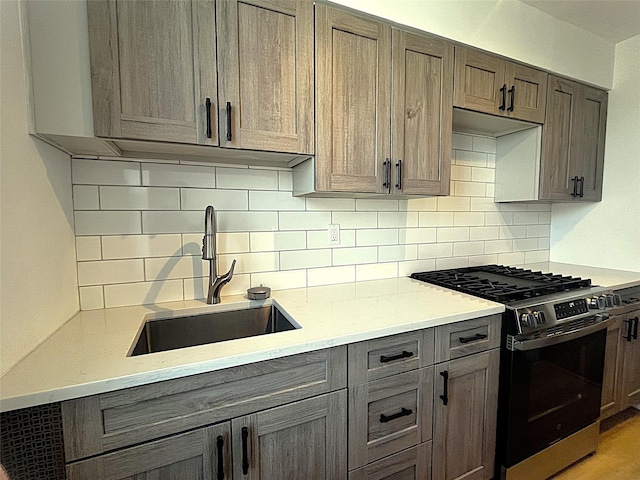 kitchen featuring stainless steel gas stove, tasteful backsplash, gray cabinets, and a sink