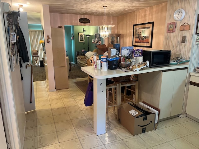 kitchen featuring black microwave, hanging light fixtures, light countertops, and a kitchen breakfast bar