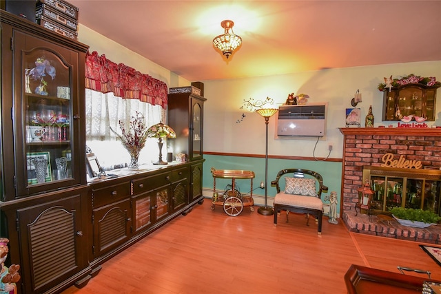 living area with a baseboard heating unit, light wood finished floors, and a brick fireplace