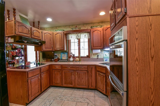 kitchen featuring brown cabinetry, light tile patterned floors, under cabinet range hood, and black electric cooktop