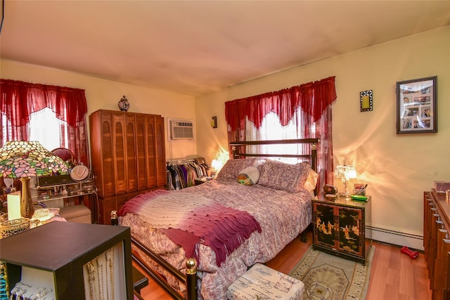 bedroom with a wall mounted air conditioner, multiple windows, baseboard heating, and wood finished floors