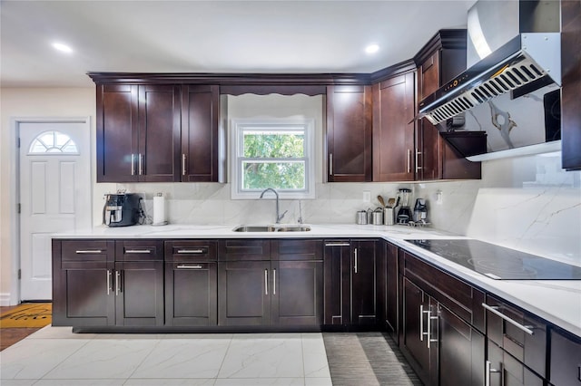 kitchen with black electric stovetop, a sink, light countertops, wall chimney range hood, and decorative backsplash