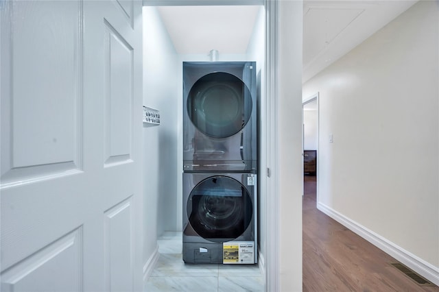 laundry room featuring laundry area, visible vents, baseboards, light wood-type flooring, and stacked washing maching and dryer