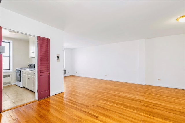 empty room with baseboards, radiator heating unit, and light wood-style floors