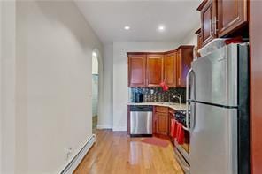 kitchen with baseboards, light wood-style floors, light countertops, appliances with stainless steel finishes, and tasteful backsplash