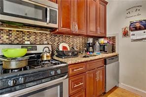 kitchen with light stone counters, decorative backsplash, appliances with stainless steel finishes, light wood-type flooring, and baseboards