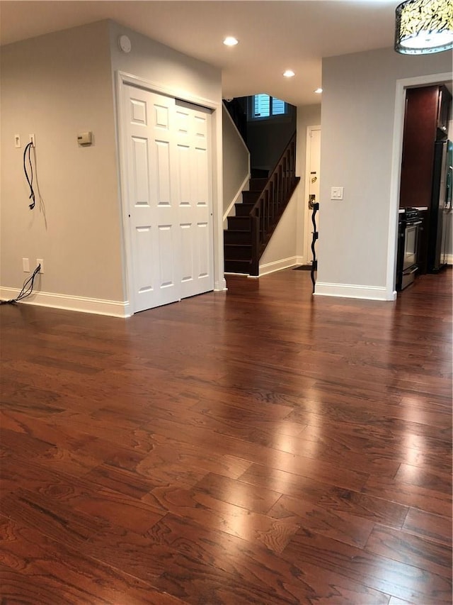 empty room with recessed lighting, dark wood finished floors, stairway, and baseboards