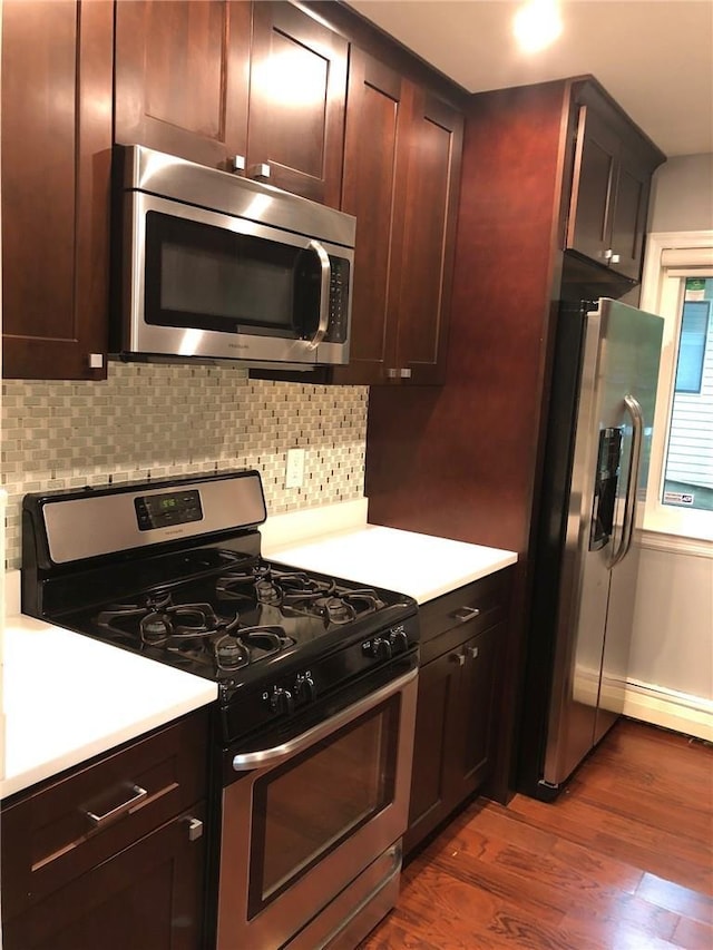 kitchen featuring decorative backsplash, dark wood-type flooring, baseboard heating, stainless steel appliances, and light countertops