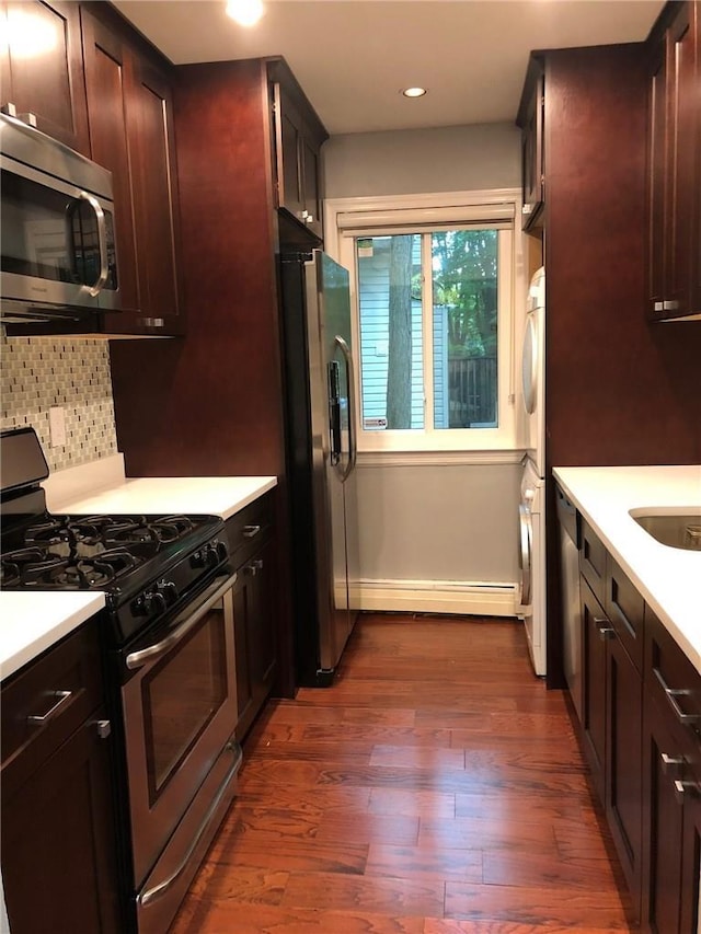 kitchen with dark wood-style flooring, light countertops, decorative backsplash, appliances with stainless steel finishes, and a baseboard heating unit