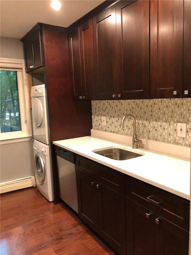 kitchen with dishwasher, stacked washer and clothes dryer, light countertops, baseboard heating, and a sink