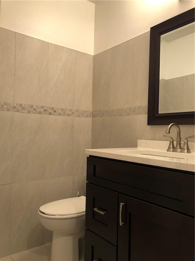 half bathroom with toilet, vanity, and tile walls