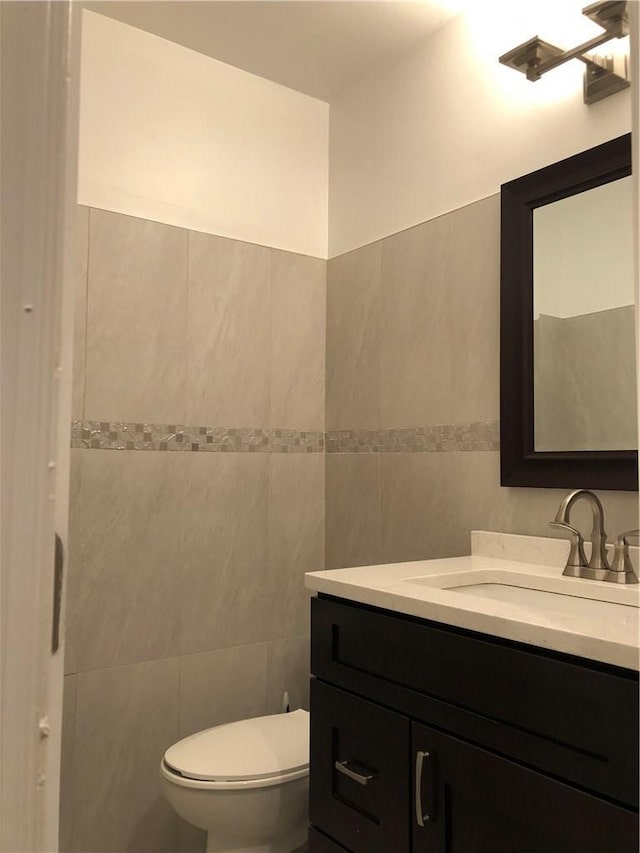 bathroom with tile walls, toilet, and vanity