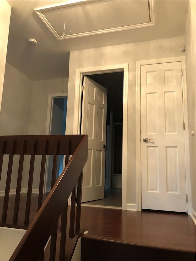 hallway featuring wood finished floors, attic access, and baseboards