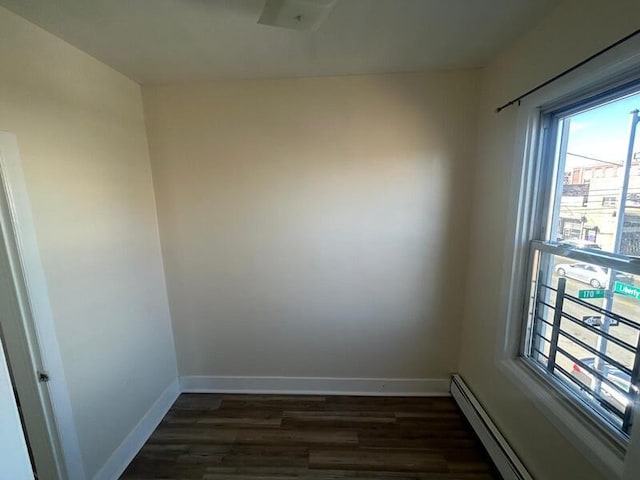 empty room featuring a baseboard radiator, baseboards, and dark wood-type flooring