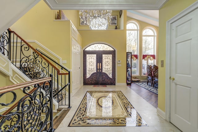 foyer featuring french doors, a towering ceiling, light tile patterned flooring, baseboards, and stairs