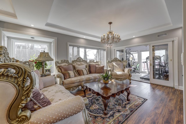 living room with a notable chandelier, visible vents, a tray ceiling, and dark wood-type flooring