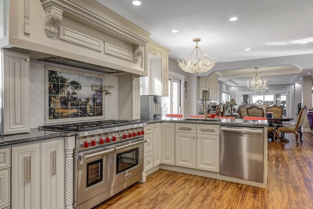 kitchen with a chandelier, stainless steel appliances, a sink, hanging light fixtures, and custom range hood