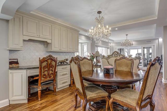 dining room featuring an inviting chandelier, ornamental molding, a raised ceiling, and light wood finished floors