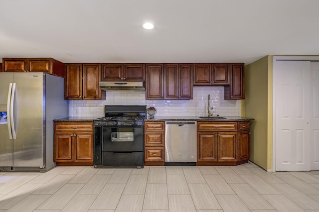 kitchen with dark stone counters, appliances with stainless steel finishes, a sink, under cabinet range hood, and backsplash