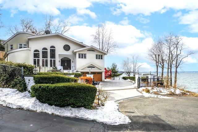 view of front facade featuring driveway, a water view, fence, and stucco siding