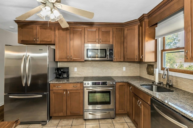 kitchen featuring appliances with stainless steel finishes, a sink, dark stone counters, a ceiling fan, and tasteful backsplash