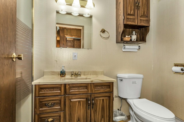 bathroom featuring vanity, toilet, and wallpapered walls