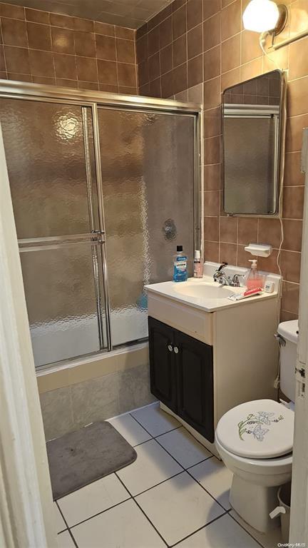 bathroom with toilet, vanity, tile walls, tile patterned floors, and a stall shower