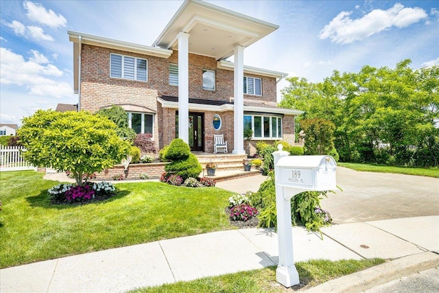 neoclassical / greek revival house featuring brick siding, driveway, and a front lawn