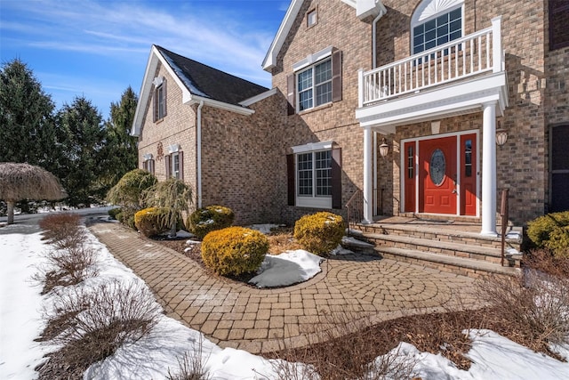 snow covered property entrance featuring a balcony and brick siding